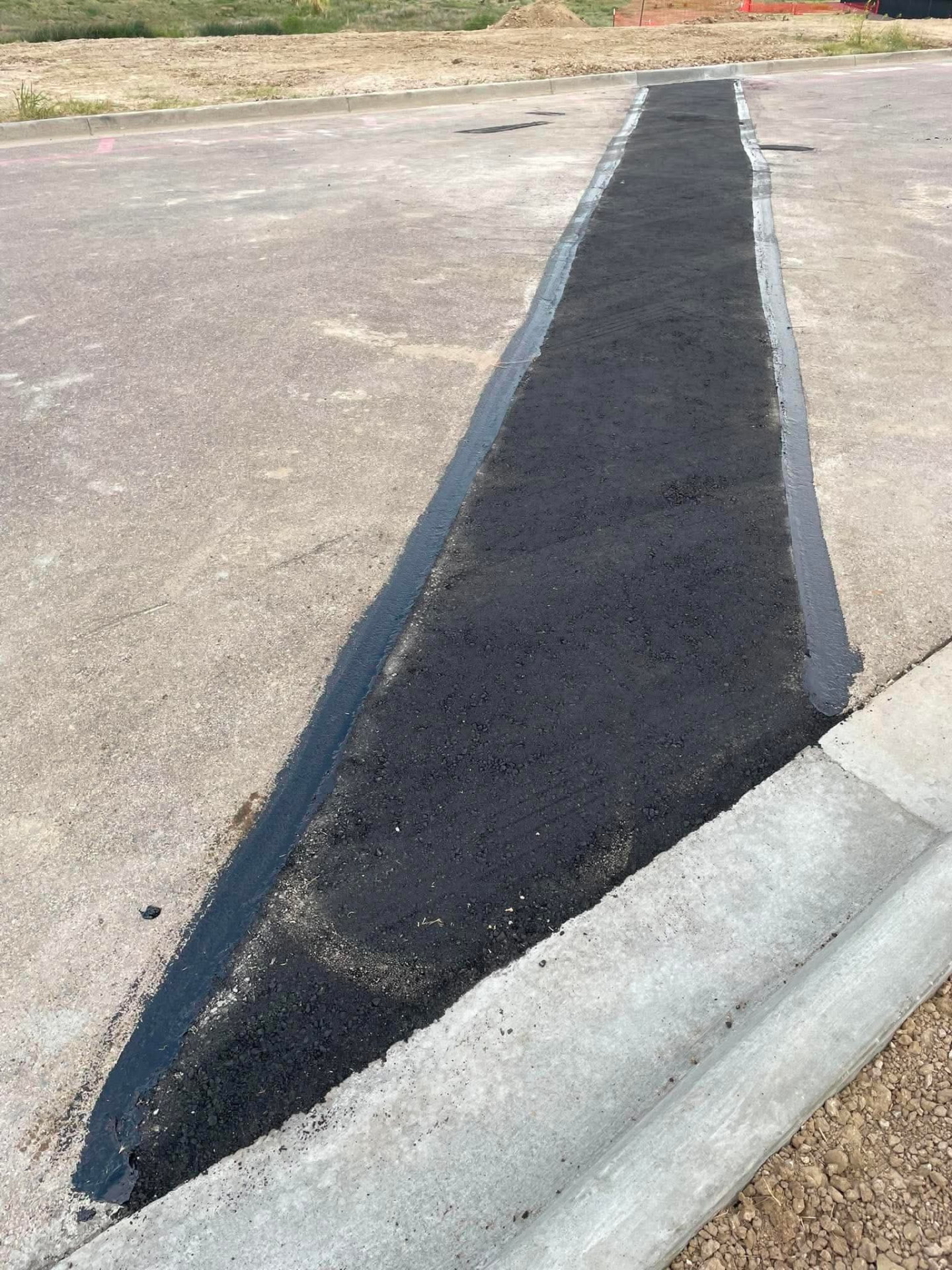 Infrared asphalt patch repair sealed along a concrete curb line