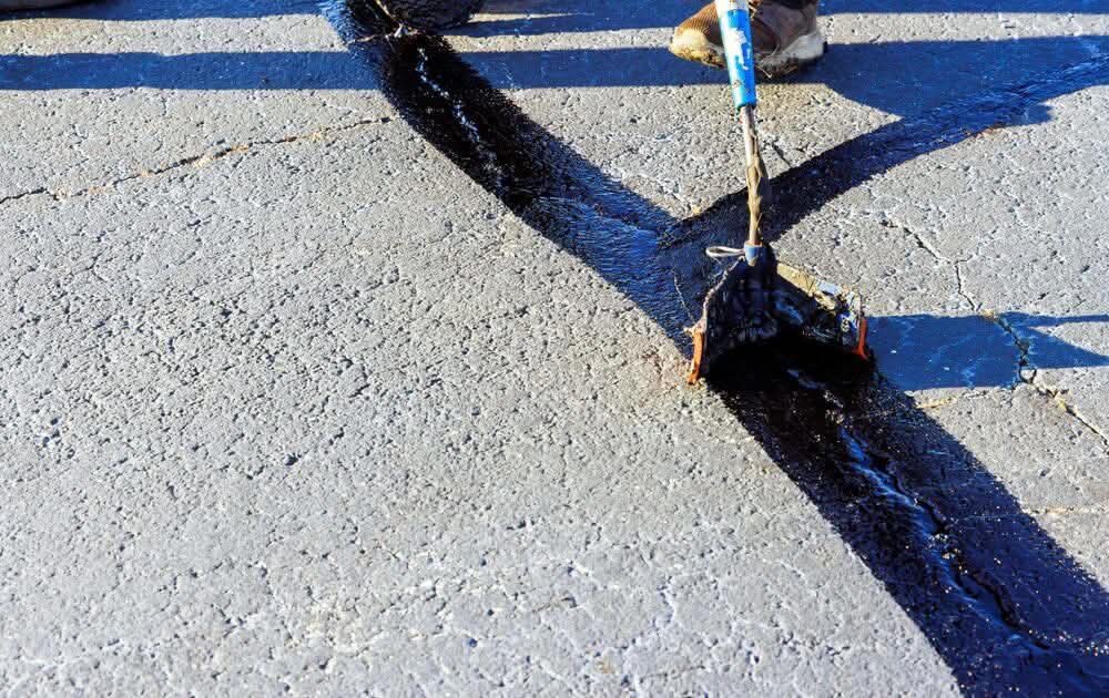 Close-up of hot rubberized crack sealing being applied to asphalt pavement